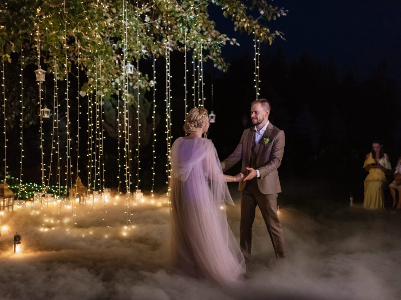 the first wedding dance of the bride and groom in the glade of the country club in the light of sunset and warm garlands